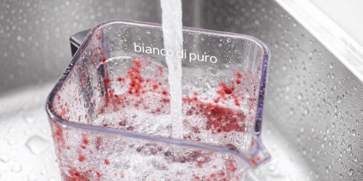 Nahaufnahme eines bianco di puro Mixerbehälters, der unter fliessendem Wasser gereinigt wird, um Fruchtreste zu entfernen.