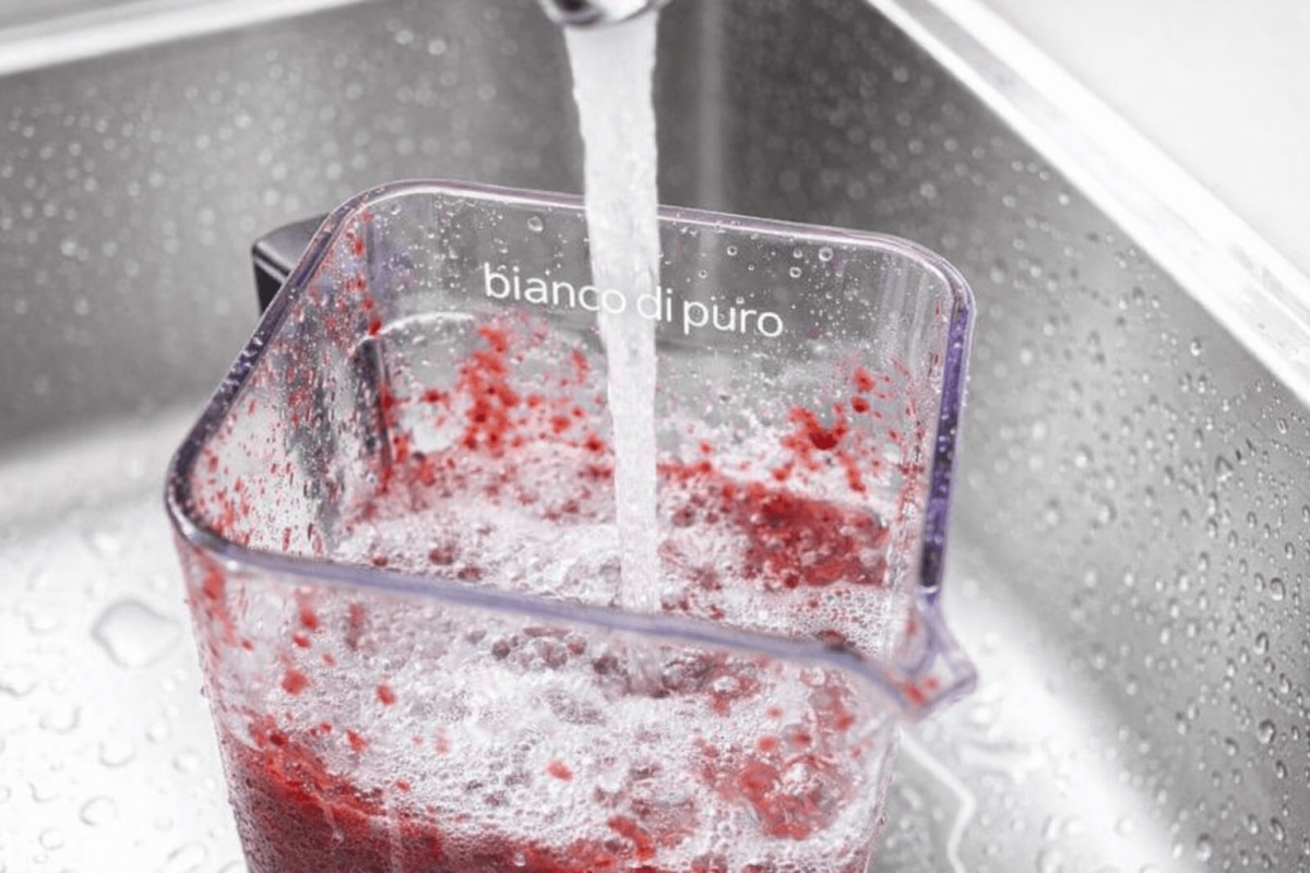Nahaufnahme eines bianco di puro Mixerbehälters, der unter fliessendem Wasser gereinigt wird, um Fruchtreste zu entfernen.