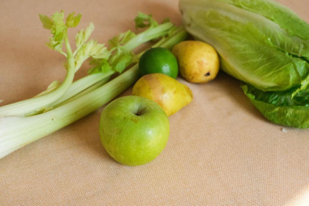 Zutaten für grünen Smoothie mit Stangensellerie und Apfel auf hellem Untergrund
