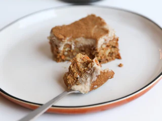 Ein Stück veganer Karottenkuchen auf einem Teller mit Gabel und Kerze im Hintergrund.