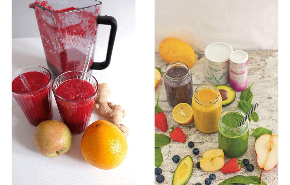 Drei Gläser mit gelben, roten und grünen Smoothies neben frischen Früchten wie Orangen, Äpfeln und Beeren.