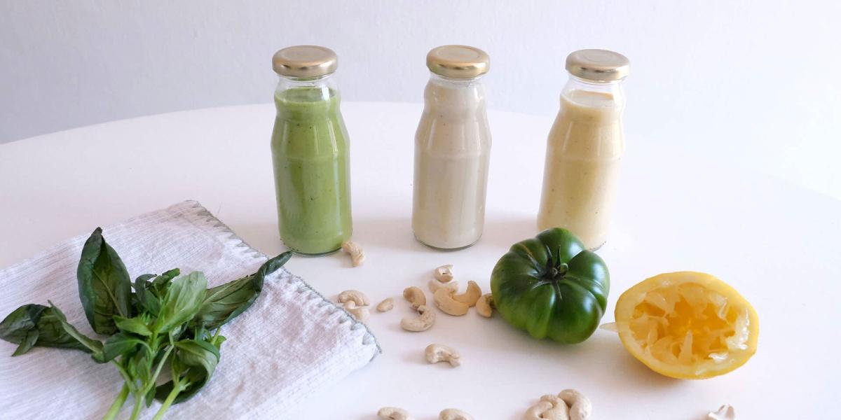 Drei verschiedene cremige Salatdressings in Glasflaschen mit Basilikum und Cashews.
