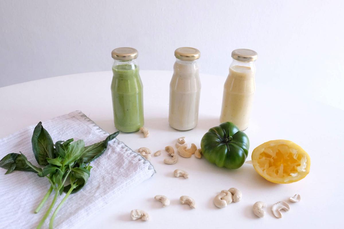 Drei verschiedene cremige Salatdressings in Glasflaschen mit Basilikum und Cashews.