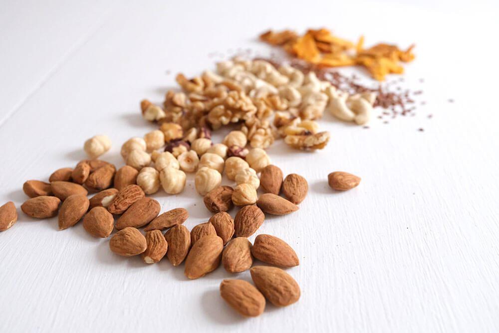 Verschiedene Nüsse wie Mandeln und Cashews sowie Leinsamen für nährstoffreiche Smoothies.
