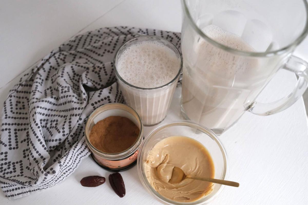 Gläser mit frischer, schäumender Nussmilch neben einer Schale mit frischem Mandelmus