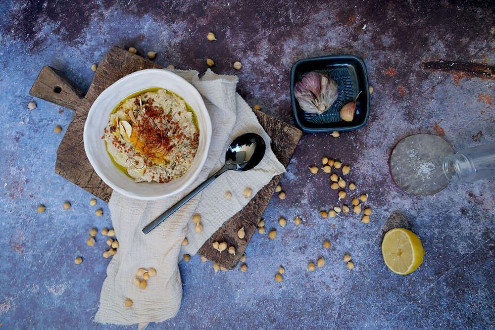 Draufsicht auf Kichererbsen, Zitrone, Knoblauch und eine Schüssel Hummus auf einer rustikalen Arbeitsfläche.